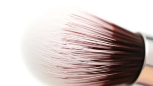 Close-up of professional makeup brush bristles showing soft, feathered synthetic fibers with metallic ferrule against clean white background, photorealistic beauty product photography