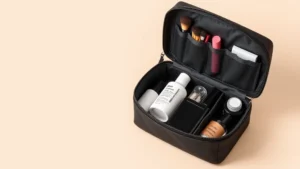 Compact cosmetic bag with waterproof lining open showing organized compartments with makeup brushes, lipstick, foundation bottle, and skincare products neatly arranged inside, neutral background, professional product photography style