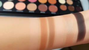 Close-up of diverse skin tones swatching neutral eyeshadow palette on forearm, natural daylight, showing color accuracy and blendability