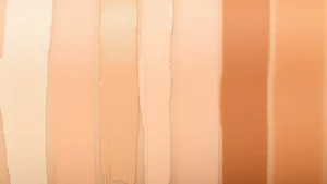 Close-up of concealer swatches displaying multiple shade variations from fair to deep skin tones, arranged in rows showing warm, neutral, and cool undertones on diverse skin samples, natural lighting