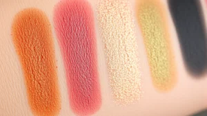 Close-up of vibrant eyeshadow palette swatches showing rich pigmentation and blend-ability on skin, featuring warm and cool tones with metallic and matte finishes
