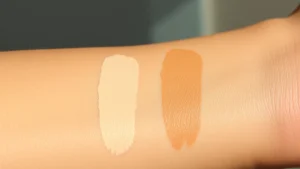 Close-up of diverse skin tones swatching creamy beige and warm tan concealer on arm, natural daylight, focusing on color accuracy and blending