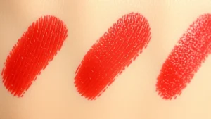Close-up of vintage 1950s lipstick swatches on skin showing rich carmine red pigment with dimensional depth, natural lighting highlighting the creamy texture and smooth application, no product packaging visible